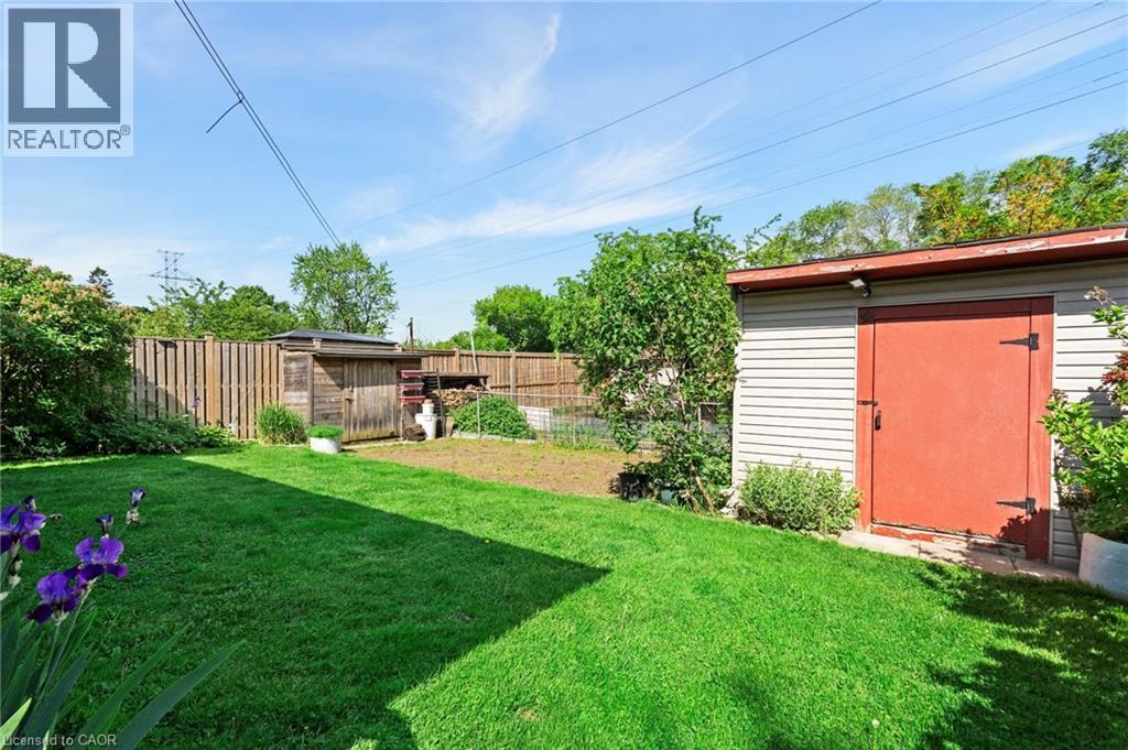 Expansive backyard featuring a manicured lawn, a detached storage shed with a vibrant red door, a secondary wooden shed, and a privacy fence - 1083 Melton Drive, Mississauga, ON