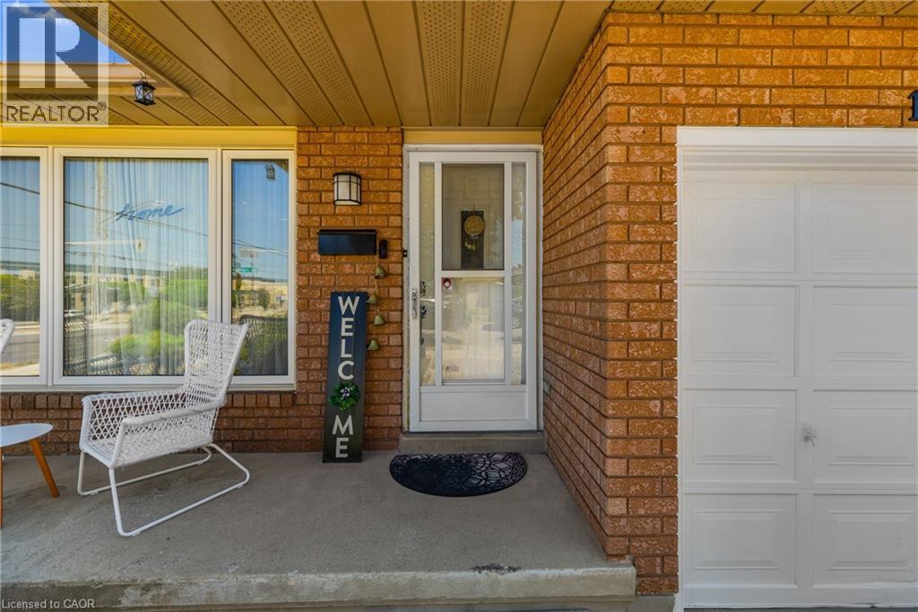 Brick exterior featuring a concrete porch, large front windows, an exterior light fixture, a black mailbox, and a paneled garage door - 102 Juniper Drive, Hamilton, ON