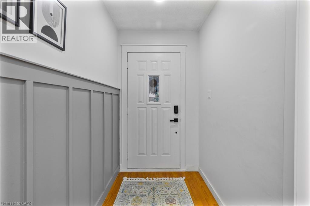 Entryway featuring rich wood-finish flooring, white walls, and a paneled accent wall - 102 Juniper Drive, Hamilton, ON