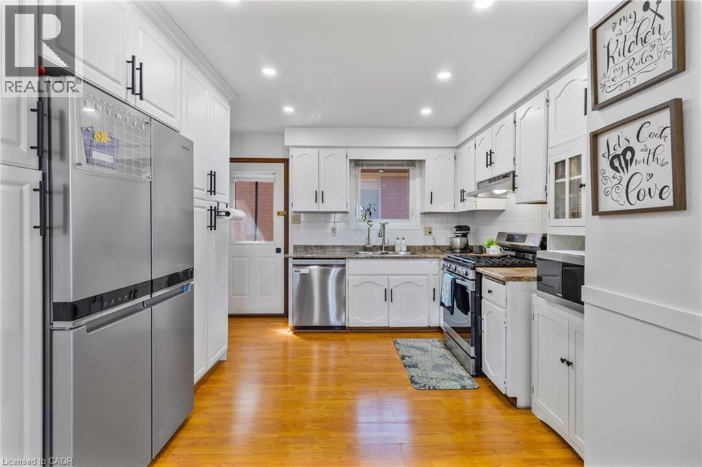 Well-appointed kitchen featuring wood-finish flooring, white cabinetry with dark hardware, stainless steel appliances, recessed lighting, and a window above the sink - 102 Juniper Drive, Hamilton, ON