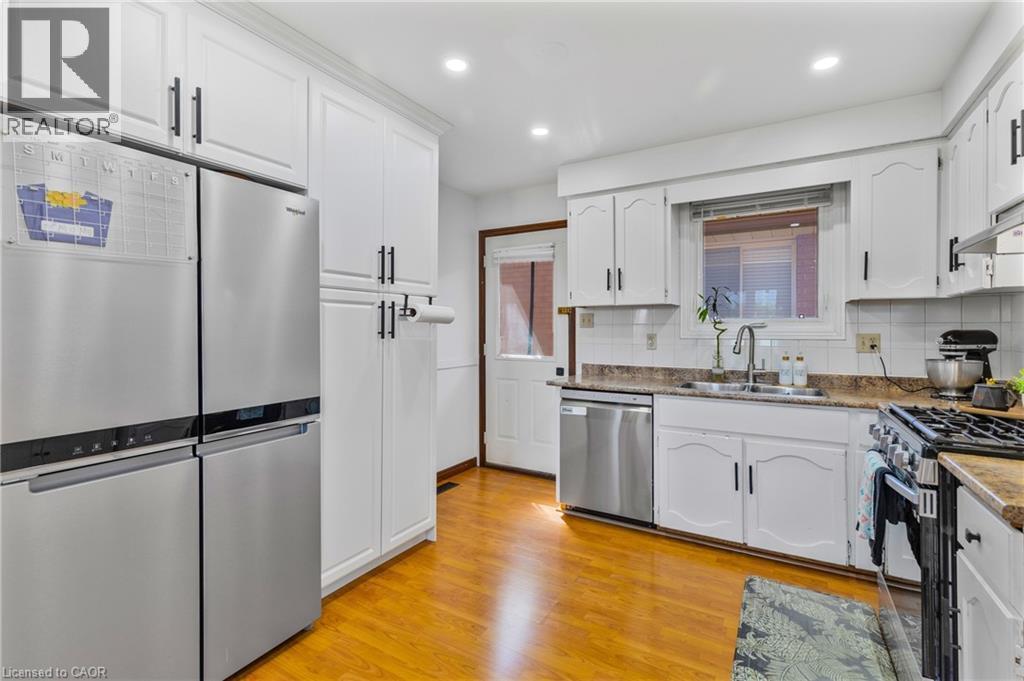 Kitchen featuring white cabinetry with dark hardware, a stainless steel refrigerator, and wood-finish flooring - 102 Juniper Drive, Hamilton, ON