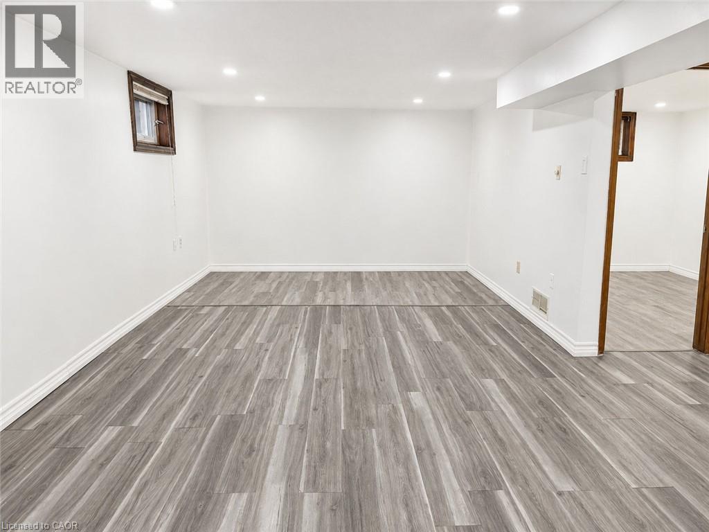Spacious room featuring light wood-finish flooring, white baseboards, and bright recessed lighting - 102 Juniper Drive, Hamilton, ON