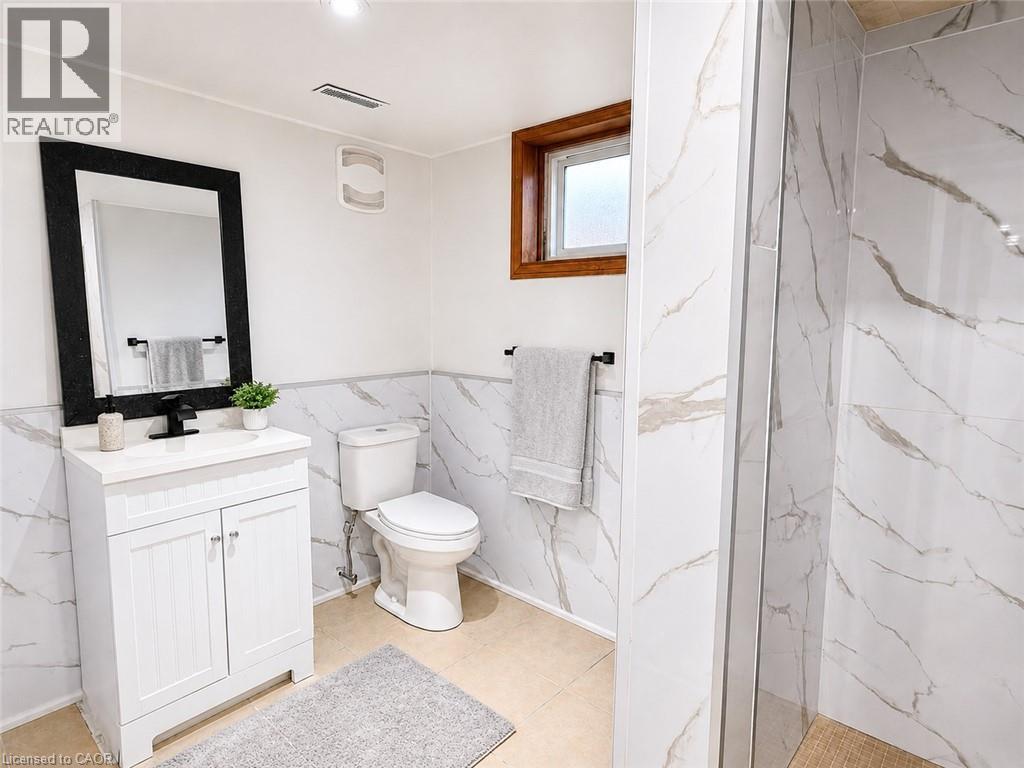 Contemporary bathroom featuring a white vanity with a black faucet, a framed mirror, and a toilet - 102 Juniper Drive, Hamilton, ON