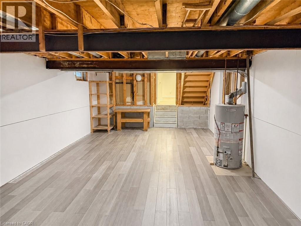 Finished basement area featuring wood-finish flooring, white paneling, exposed ceiling joists, and a partial staircase - 102 Juniper Drive, Hamilton, ON