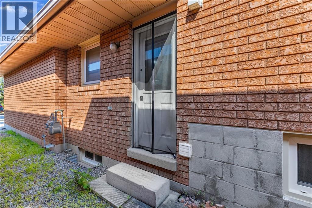 Red brick exterior with a side entry door, concrete steps, and a white window trim - 102 Juniper Drive, Hamilton, ON