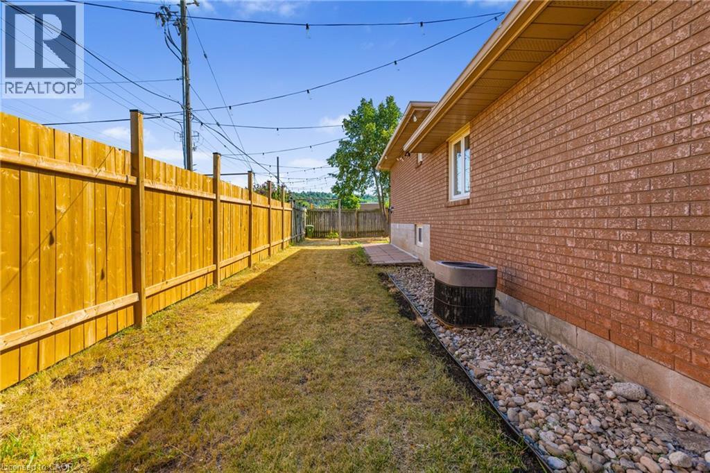Expansive side yard featuring a new wood privacy fence, brick exterior, and decorative rock landscaping - 102 Juniper Drive, Hamilton, ON
