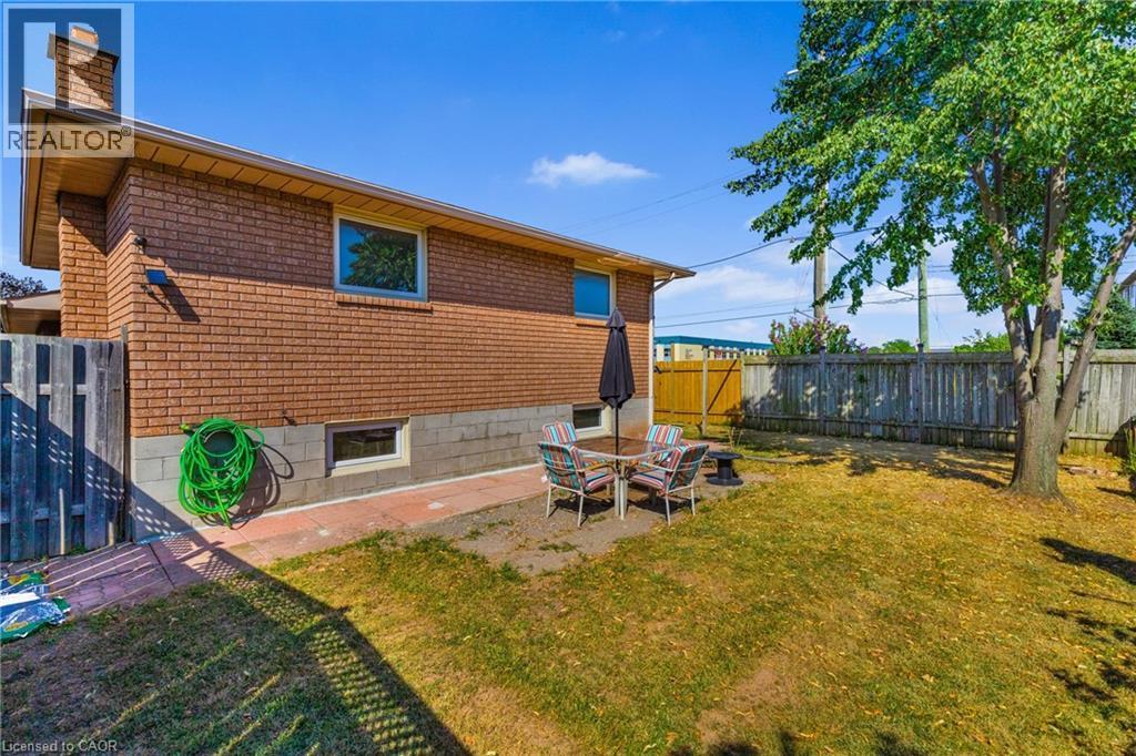 Rear exterior featuring red brick siding, a brick chimney, and a wooden privacy fence - 102 Juniper Drive, Hamilton, ON