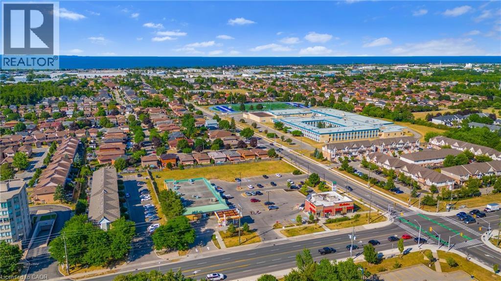Expansive aerial perspective showcasing a residential area with a prominent institutional building featuring a sports field - 102 Juniper Drive, Hamilton, ON
