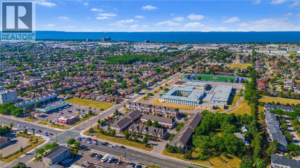 Aerial perspective showcasing a developed community with a prominent institutional building, multiple residential areas, and commercial storefronts - 102 Juniper Drive, Hamilton, ON