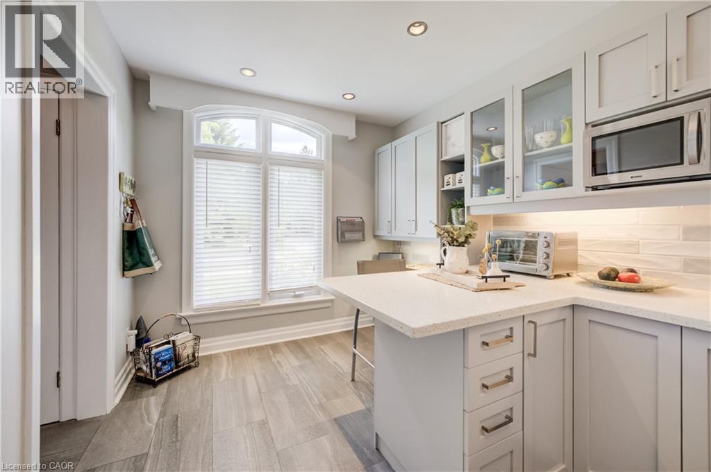 Kitchen featuring a large arched window with blinds, light wood-finish flooring, recessed ceiling lighting, light gray cabinetry with glass-front uppers. - 314 Glasgow Street, Kitchener, ON