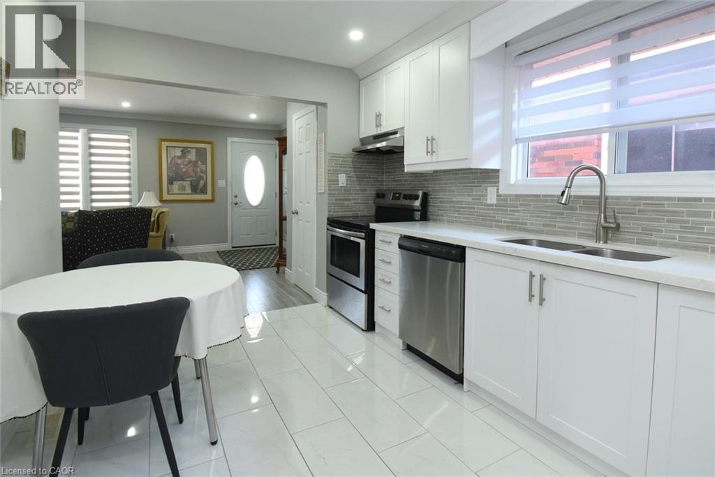 Contemporary kitchen featuring white cabinetry, stainless steel appliances, a tile backsplash, light-toned countertops, and recessed lighting - 185 Rosslyn Avenue N, Hamilton, ON - Indoor Photo Showing Kitchen With Double Sink