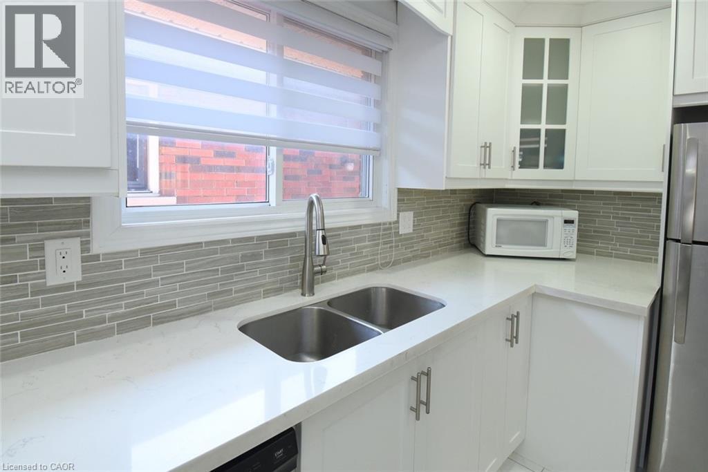 Kitchen featuring a double basin stainless steel sink with a high-arc faucet, quartz countertops, and a full tile backsplash - 185 Rosslyn Avenue N, Hamilton, ON - Indoor Photo Showing Kitchen With Double Sink