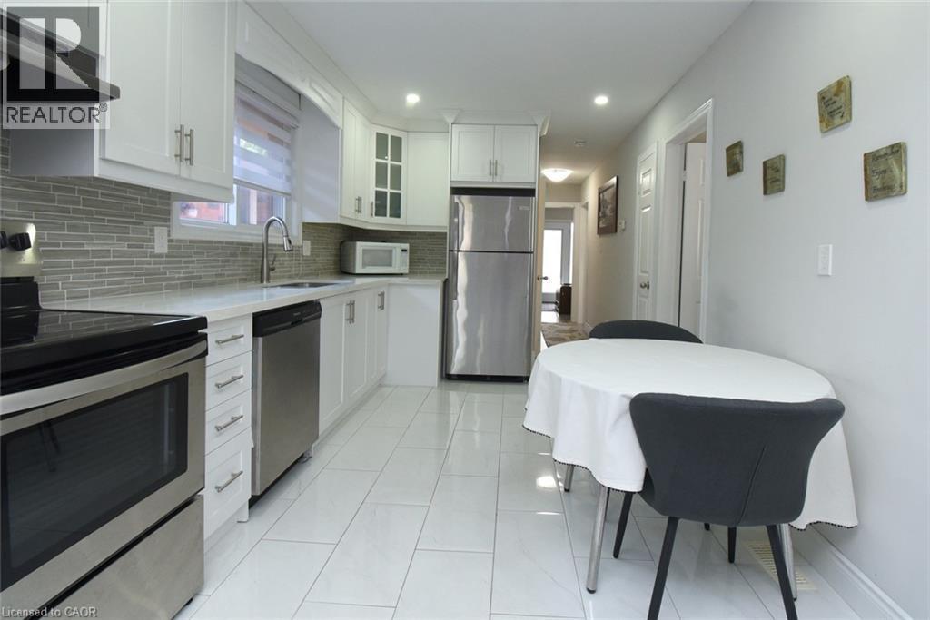 Modern kitchen featuring white cabinetry, stainless steel appliances, a tile backsplash, light countertops, and tile flooring - 185 Rosslyn Avenue N, Hamilton, ON - Indoor Photo Showing Kitchen