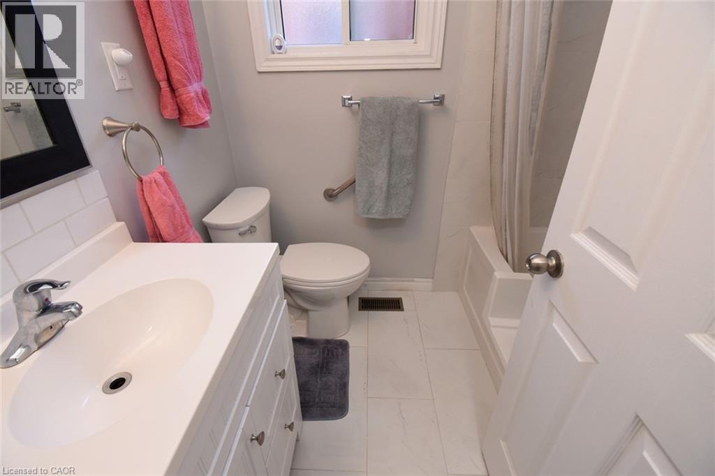 Bathroom featuring a white vanity with integrated sink, chrome faucet, white subway tile backsplash, and a white toilet - 185 Rosslyn Avenue N, Hamilton, ON - Indoor Photo Showing Bathroom