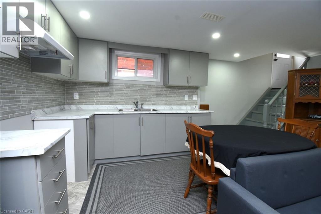 Kitchenette featuring grey cabinetry, a light-toned countertop, and a mosaic tile backsplash - 185 Rosslyn Avenue N, Hamilton, ON - Indoor Photo Showing Kitchen With Double Sink