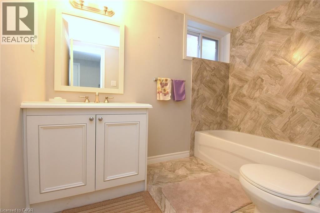 Bathroom featuring a white vanity with panel cabinetry, a rectangular mirror, a bathtub with a tiled surround, and a coordinating tiled floor - 185 Rosslyn Avenue N, Hamilton, ON - Indoor Photo Showing Bathroom