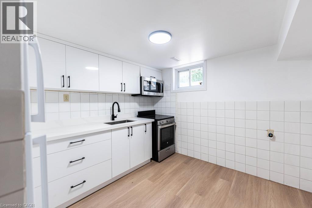Kitchen featuring white cabinetry with matte black hardware, white countertops, a stainless steel range, and a coordinating microwave - 65 Garden Crescent Unit# Lower, Hamilton, ON - Indoor Photo Showing Kitchen
