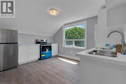 Kitchen area featuring wood-finish flooring, white cabinetry, a stainless steel refrigerator, and a double basin sink with a high-arc faucet -