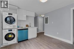Compact kitchen area featuring a stacked washer and dryer unit, flat-panel white cabinetry, a single basin sink with a chrome faucet, and a built-in dishwasher -