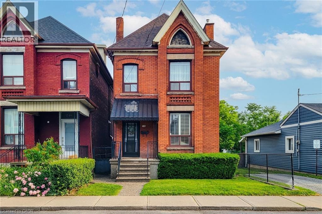 Brick facade residence featuring a steep gabled roof, arched window detailing, and a prominent front entrance with a metal awning - 244 Hughson Street N, Hamilton, ON