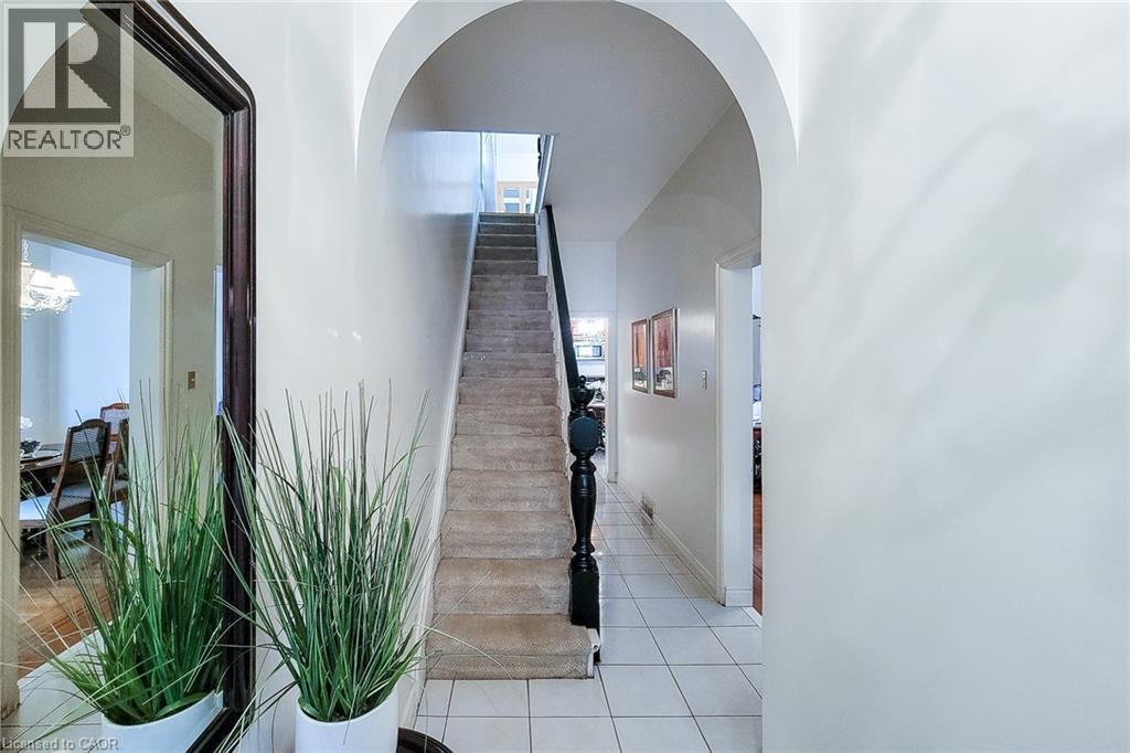 Archway entry hallway featuring white tile flooring and a carpeted staircase with a dark wood baluster - 244 Hughson Street N, Hamilton, ON
