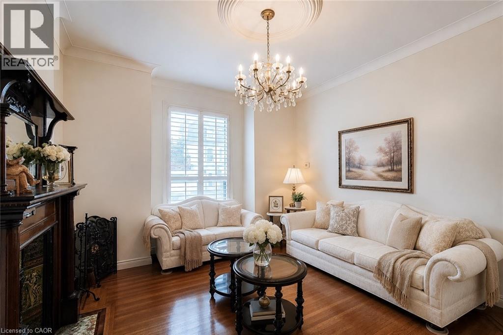 Living area featuring rich wood-finish flooring, an ornate chandelier with ceiling medallion, and crown molding - 244 Hughson Street N, Hamilton, ON