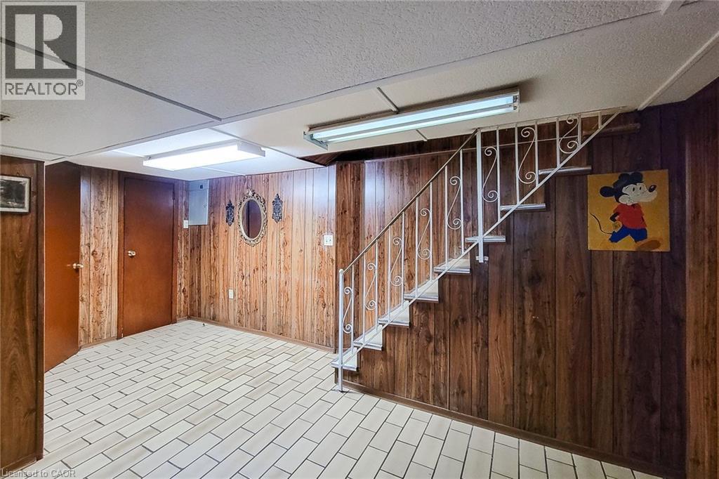 Lower level featuring wood-panel walls, white floor tiles, and a staircase with a decorative metal railing - 244 Hughson Street N, Hamilton, ON