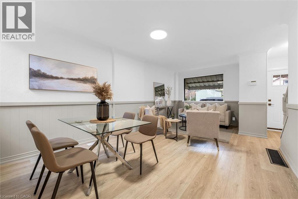 Open-concept living area featuring light wood-finish flooring, white and light grey wainscoting, a large front window, recessed lighting, and a white entry door with a frosted glass pane - 11 Ford Street, Hamilton, ON