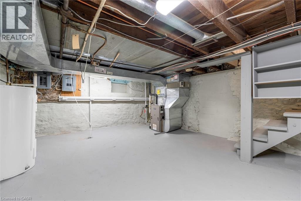 Basement area featuring a light gray floor, white painted stone foundation walls, exposed ceiling joists, and a built-in staircase with shelving - 11 Ford Street, Hamilton, ON