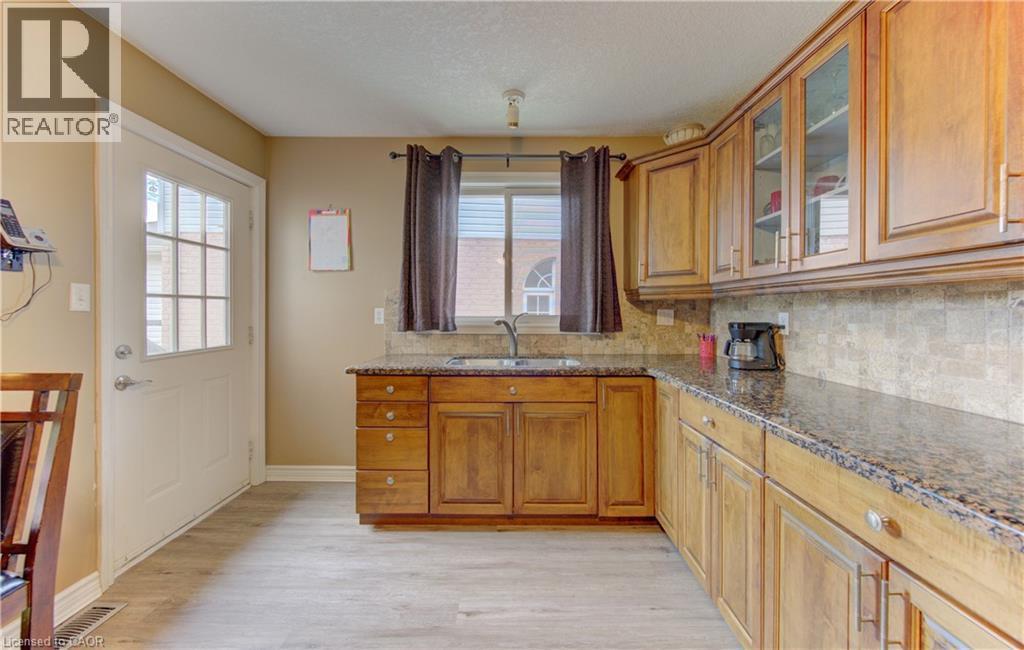 Kitchen featuring wood-finish flooring, L-shaped cabinetry with glass-front uppers, granite countertops, tile backsplash, and a window above the sink - 599 Coldstream Drive, Waterloo, ON