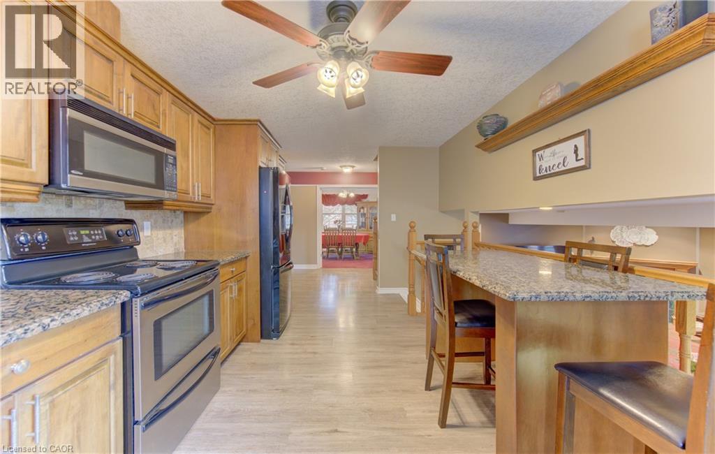 Kitchen featuring wood cabinetry, light-toned wood-finish flooring, stainless steel appliances, granite countertops, and a breakfast bar with wood paneling - 599 Coldstream Drive, Waterloo, ON