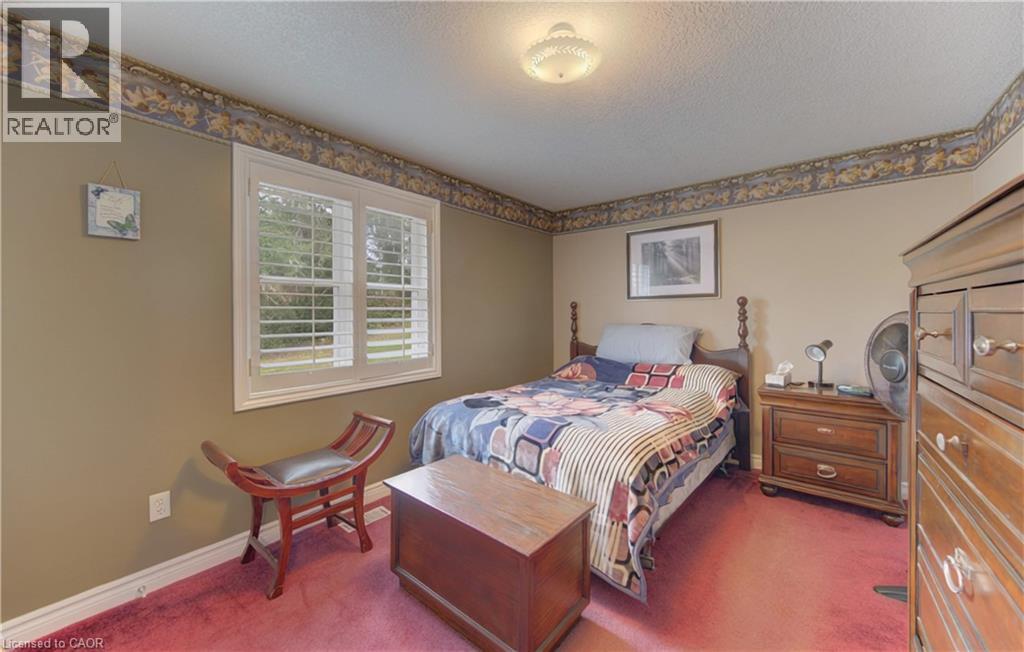 Bedroom featuring a window with white louvered shutters, light beige painted walls, a decorative border, and red carpet flooring - 599 Coldstream Drive, Waterloo, ON
