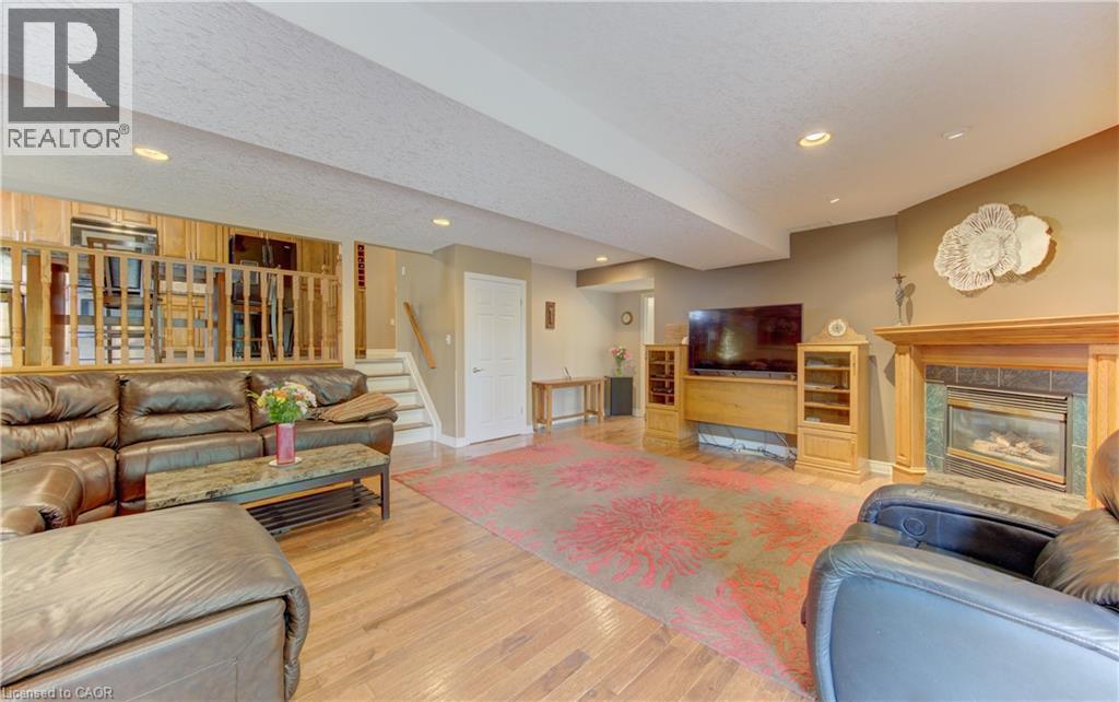 Spacious recreation room featuring wood-finish flooring, a built-in fireplace with a stone surround and wood mantle, and recessed lighting - 599 Coldstream Drive, Waterloo, ON