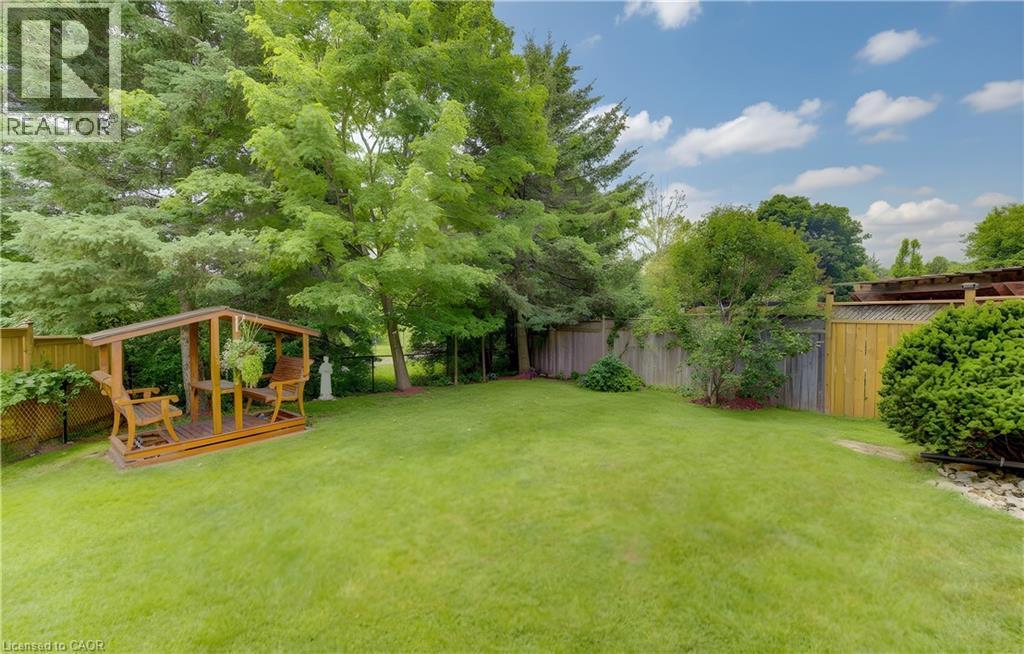 Expansive green lawn with a wooden gazebo, surrounded by mature trees and a privacy fence - 599 Coldstream Drive, Waterloo, ON