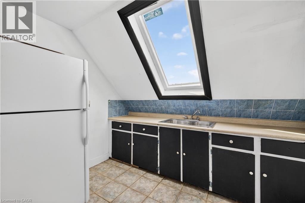 Kitchenette area featuring a large skylight, a stainless steel double basin sink, blue tile backsplash, light-toned countertops, and black cabinetry with white knob hardware - 26 Arthur Avenue, St. Thomas, ON - Indoor Photo Showing Kitchen