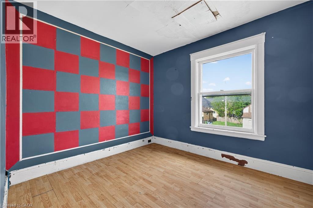 Interior room featuring wood-finish flooring, a checkerboard accent wall, and a single window with white trim - 26 Arthur Avenue, St. Thomas, ON - Indoor Photo Showing Other Room
