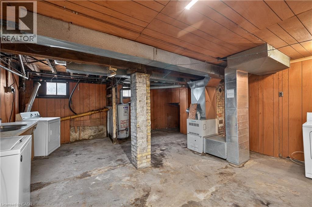 Basement area featuring wood paneling, exposed brick support column, concrete flooring, and visible utility systems - 26 Arthur Avenue, St. Thomas, ON - Indoor Photo Showing Basement
