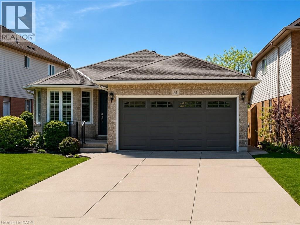 Brick exterior with a dark garage door, bay window, and a paved driveway - 51 Redtail Crescent, Hamilton, ON