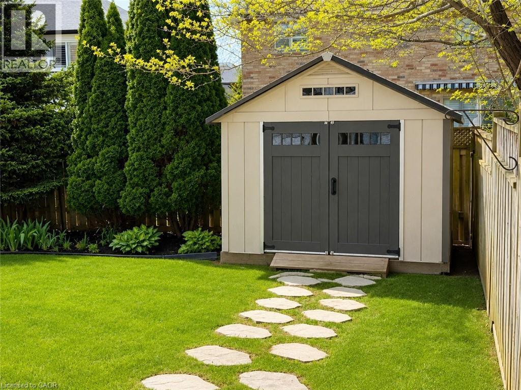 Cream-colored shed with dark gray double doors, transom windows, and a dark shingle roof - 51 Redtail Crescent, Hamilton, ON
