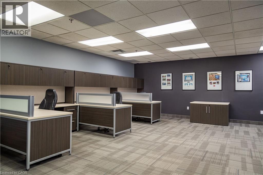 Open-plan office area featuring modular workstations with privacy panels, wood-finish cabinetry, and suspended acoustic ceiling tiles with integrated lighting - 5100 South Service Road, Burlington, ON