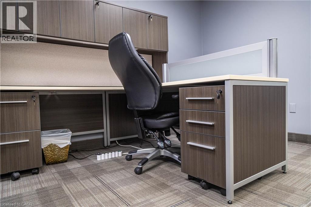 Modern office workstation featuring wood-finish cabinetry, integrated overhead storage, and a frosted glass partition - 5100 South Service Road, Burlington, ON