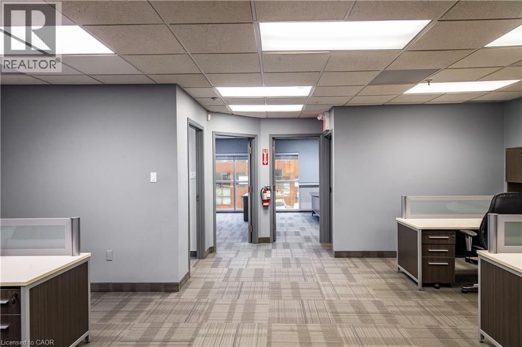 Open-concept workspace featuring patterned carpet flooring, neutral gray walls, and drop ceiling with integrated lighting - 5100 South Service Road, Burlington, ON