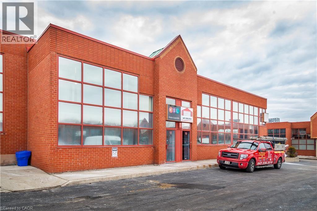 Brick commercial building featuring large grid-pane windows, a prominent gable facade, and a paved parking area - 5100 South Service Road, Burlington, ON