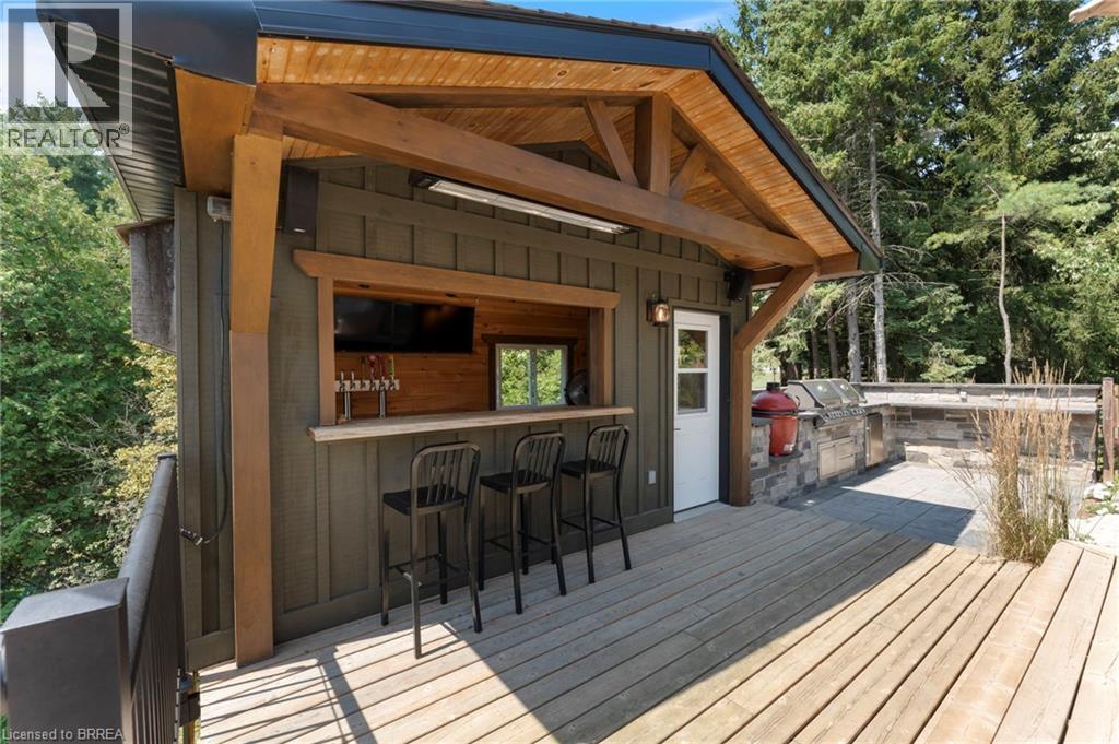 Outdoor structure featuring a covered bar area with a serving window, a built-in outdoor kitchen with stone veneer base, and a wooden deck - 182 Governors Road E, Paris, ON