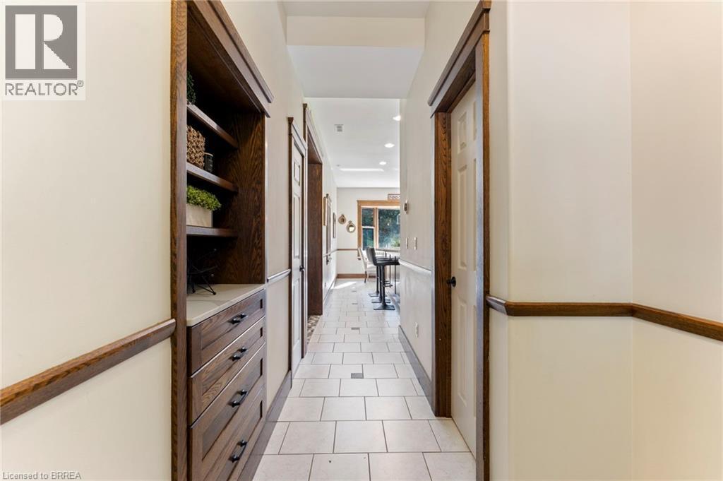 Hallway featuring light-toned tile flooring with dark accent tiles, built-in wooden cabinetry with open shelving and drawers, white panel doors, and rich wood trim - 182 Governors Road E, Paris, ON