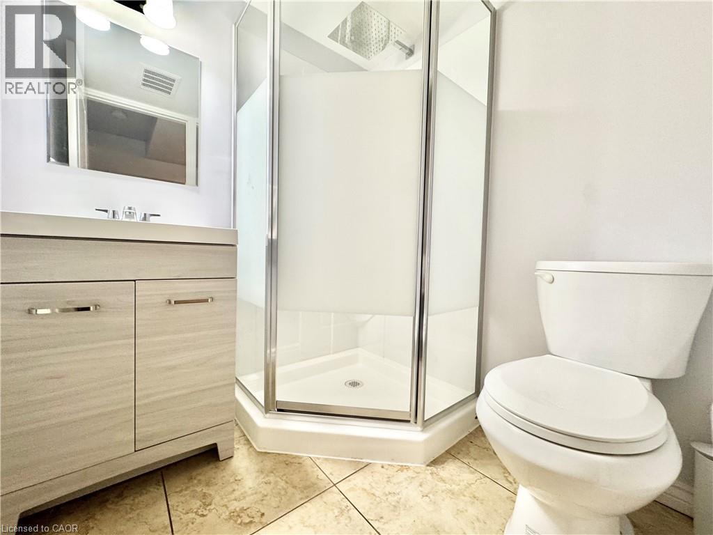 Corner shower with clear glass enclosure and frosted panels, complemented by a wood-finish vanity with a rectangular sink and chrome faucet - 1333 Countrystone Drive, Kitchener, ON