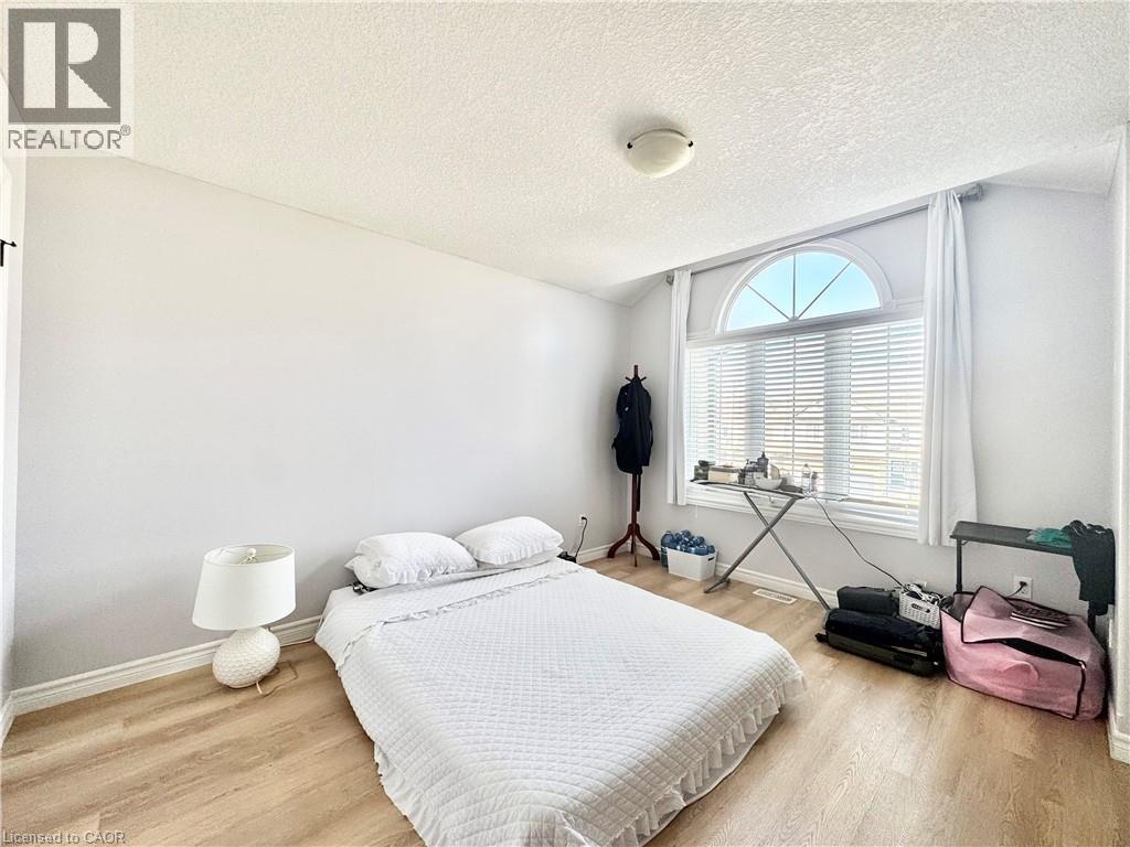 Room featuring an arched window with integrated blinds and white drapes, wood-finish flooring, and light-toned walls - 1333 Countrystone Drive, Kitchener, ON