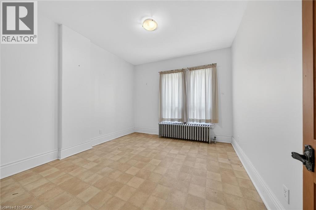 White-walled room featuring a checkered floor, built-in radiator, and central ceiling light fixture - 16 Mulberry Street, Hamilton, ON