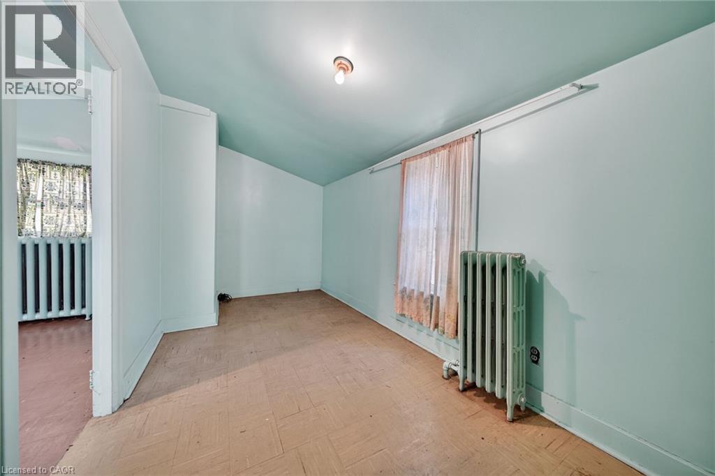 Room featuring an angled ceiling, window with a radiator below, and parquet-style flooring - 16 Mulberry Street, Hamilton, ON
