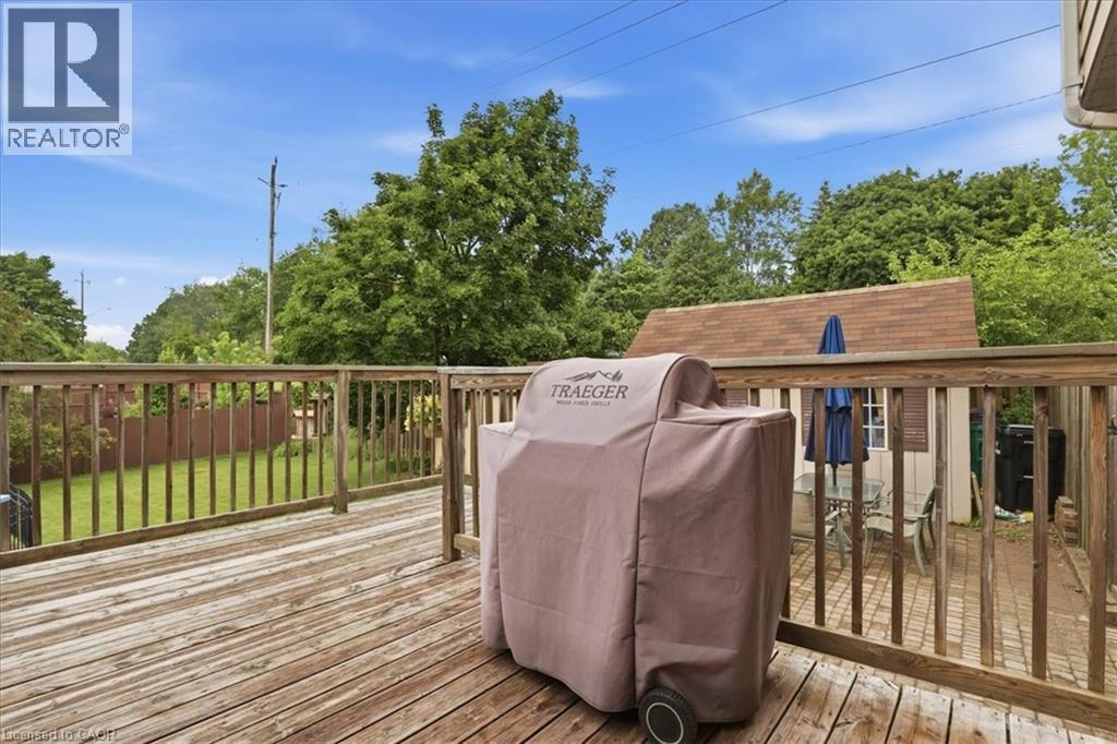 Wood-finish deck with railing, featuring a detached shed with a shingled roof, a paved patio, and a grass lawn beyond a wood fence - 116 Scott Road, Cambridge, ON